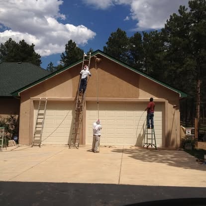 Confident Coatings crew working on a stucco garage exterior with ladders